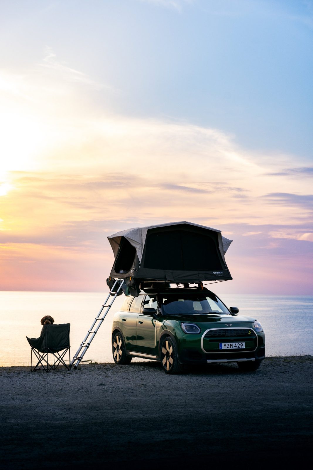 Car with an open roof tent by the sea at sunset