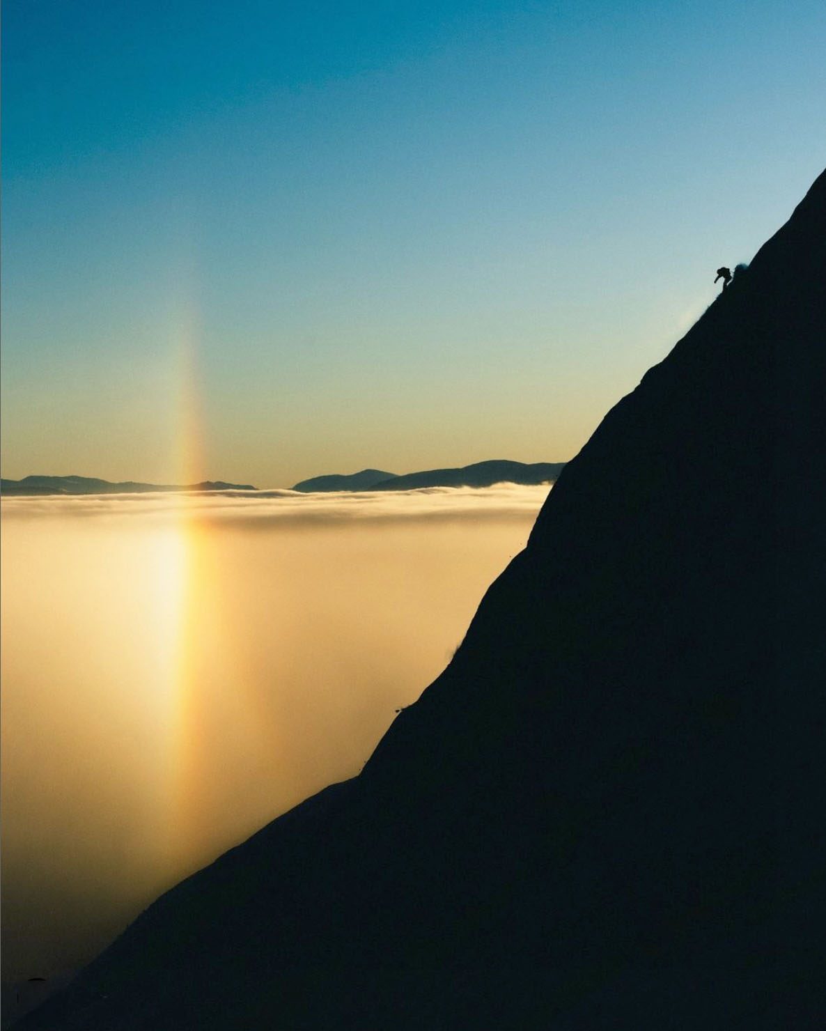 Climber silhouetted against a sun pillar above the clouds